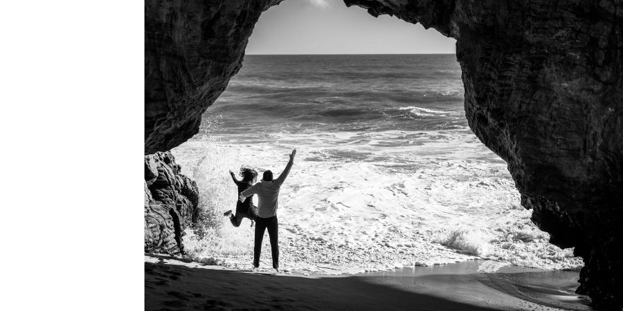 B&W jumping under the natural bridge as waves come in - Panther Beach Santa Cruz and Quail Hollow Felton engagement photography - Sara and Scott - photos by Bay Area wedding photographer Chris Schmauch